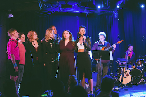 Six Broadway stars gather on stage to sing with a band playing on stage behind them